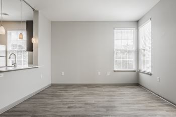 A spacious room with a kitchen area to the left and a large window with blinds on the right wall.